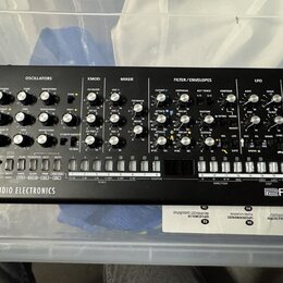 Černý syntezátor s nápisem SE-02 STUDIO ELECTRONICS a logem Roland. Přední panel obsahuje množství otočných potenciometrů, tlačítek a přepínačů rozdě…