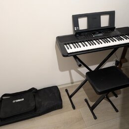 Černý digitální klavír umístěný na černém skládacím stojanu s přívodním kabelem. Na nástroji je vidět nápis YAMAHA a doprovodná hudební notová opěrka…