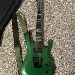 Zelená elektrická kytara s kovovými strunami a dvěma černými humbuckery. Na hlavě je viditelné logo Ibanez. Kytara má zelený popruh a vedle ní leží č…