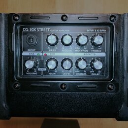 Kytarový zesilovač s černým povrchem a ovládacím panelem. Na panelu je nápis CG-10X STREET GUITAR AMPLIFIER a BATTERY & AC SUPPLY. Ovládání obsahuje…