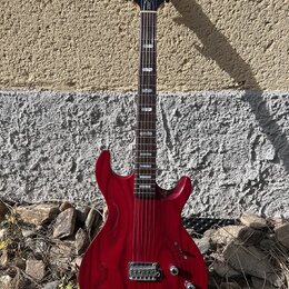 Červená elektrická kytara s výraznou strukturou dřeva na povrchu. Na hlavě je viditelné logo Line 6 a nápis LINE 6. Nástroj má dva humbuckery, tři ov…