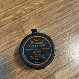 Kulatá černá plastová nádobka s oranžovým potiskem. Na víčku je logo koruny a nápisy REMO, PUTTY PAD, To Remove, Squeeze Container, NON-TOXIC, REMO,…