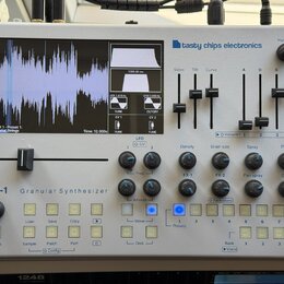 Stříbrný granulární syntetizátor s nápisem GR-1 Granular Synthesizer a logem tasty chips electronics. Zařízení má displej s vizualizací vlnovky, něko…