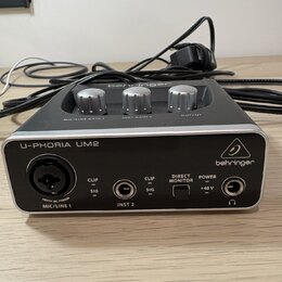 Kompaktní zvuková karta v šedé barvě s kovovým povrchem. Na přední straně je nápis U-PHORIA UM2 a logo behringer. Jsou zde vidět vstupy MIC/LINE 1 (X…