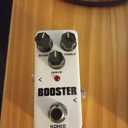 Bílý kytarový efekt s nápisem BOOSTER a značkou KOKKO. Na horní straně jsou tři černé otočné knoflíky s popisky BASS, DRIVE a TREBLE. Uprostřed se na…