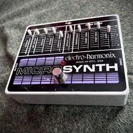 Kytarový efekt v bílém šasi s černým horním panelem. Na panelu je nápis MICROSYNTH a logo electro-harmonix s doplňkem MADE IN NYC, USA. Horní část ob…