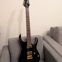 Černá elektrická kytara s tmavým hnedým hmatníkem a zlatým hardwarem. Na hlavě je bílý nápis Ibanez. Kytara má dva humbuckery, dvě otočné potenciomet…