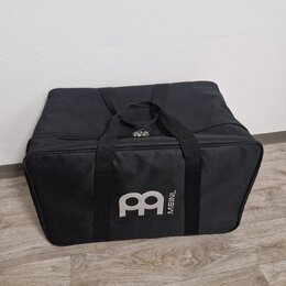 Černá textilní přepravní taška s dvěma rukojtěmi a zipem. Na přední straně je šedé logo ve tvaru stylizovaného písmena M a svislý nápis MEINL. Povrch…
