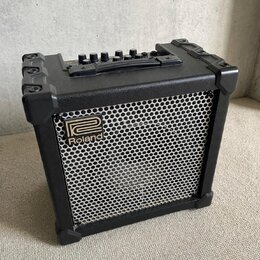 Černý kompaktní kombo zesilovač s kovovou mřížkou reproduktoru. Na přední straně je umístěno logo a nápis Roland. Horní panel obsahuje ovládací knofl…