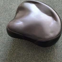 Černý polstrovaný sedák v ergonomickém tvaru. Povrch je z hladkého materiálu s viditelným prošíváním po okraji. Na fotce nejsou žádné viditelné značk…