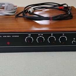 Stereo zesilovač v dřevěném šasi s černým čelním panelem. Na panelu je nápis MODEL AZS 100 L STEREO a logo TESLA. Jsou zde čtyři otočné ovladače, něk…