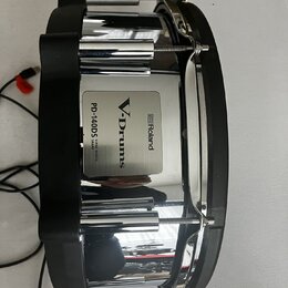 Elektronický snare s chromovaným kovem a černými plastovými prvky. Na boku je vidět stříbrný štítek s nápisy Roland, V-Drums a PD-140DS V-PAD DIGITAL…