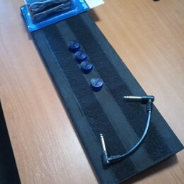 Na černém podkladu leží krátký černý audio kabel s 6,3mm jack konektory na obou koncích. Vedle něj jsou čtyři modré plastové krytky a v horní části j…