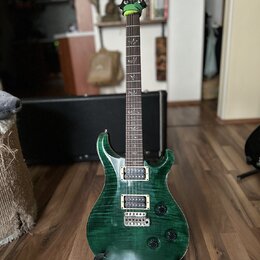 Zelená elektrická kytara s výraznou strukturou dřeva na těle a hnedým hmatníkem. Na hlavě je viditelné logo PRS. Kytara má dva humbuckery, fixační mo…