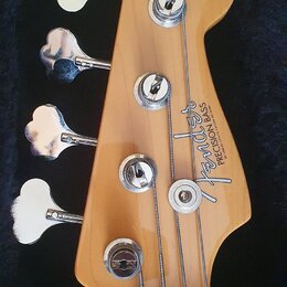 Hlava čtyřstrunné basové kytary z přírodního dřeva v černém kufru. Na hlavě je vidět logo Fender a nápis PRECISION BASS, pod kterým je drobný nečitel…