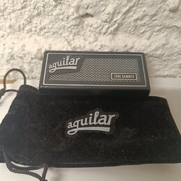 Černý kytarový pedál s nápisem aguilar a označením TONE HAMMER. Je vyroben z kovu s texturovaným povrchem a obsahuje stříbrnou mřížku. Vedle pedálu j…