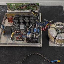 Fotografie zachycuje vnitřek elektronického zařízení, pravděpodobně zesilovače, bez krycího šasi. Je vidět hliníkový základ s instalovanými kondenzát…