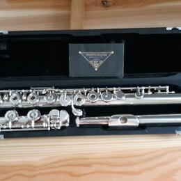 Stříbrná flétna v černém pevném kufru. Na krabičce uvnitř kufru je nápis SANKYO FLUTES, MFG. CO., LTD. JAPAN a pod ním trojúhelníkové logo. Nástroj v…