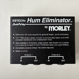 Černý box s nápisem EBTECH® Hum Eliminator™ by MORLEY®. Na povrchu je text popisující funkce zařízení a poznámka Made in U.S.A. V dolní části jsou dv…