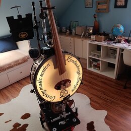 Na fotografii je hybridní nástroj kombinující kontrabas a buben. Na bílém bubnovém povrchu je černý nápis „Country music session Kontrabass Banjo“. N…