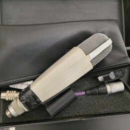 V černém kufru s pěnovou výplní leží mikrofon v krémovém provedení s kovovou mřížkou. Vedle něj je umístěn kabel s konektorem XLR a černý plastový ad…