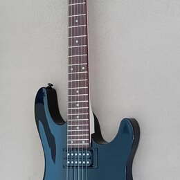 Elektrická kytara s tmavě modrým lakovaným tělem a hnědým hmatníkem. Na hlavě je bílé logo Cort. Nástroj má dva humbuckery, fixační most a dvě ovláda…