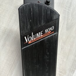 Černý volume pedál s žebrovaným povrchem. Na horní části je bílý nápis VOLUME a červený nápis MONO, pod kterými jsou dvě červené vlnovky. V horní čás…