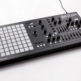 Černý hybridní syntetizátor s bílou mřížkou 8x8 podsvícených polí vlevo. Na horní části je bílý nápis MEDUSA HYBRID SYNTHESIZER a v pravém dolním roh…