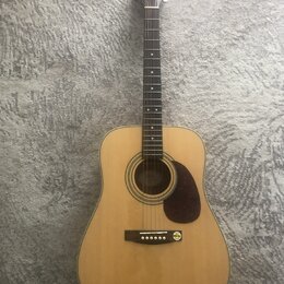 Akustická kytara s přírodním dřevem na lícové desce a tmavým hnedým pickguardem. Na hlavě je viditelné logo Carl. Nástroj vykazuje čistý povrch bez v…