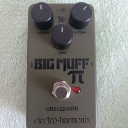 Šedý kytarový efekt s nápisy BIG MUFF π, ОВЕРДРАЙВ a electro-harmonix. Na horní straně jsou tři černé otočné knoflíky s popisky SUSTAIN, TONE a VOLUM…