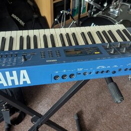 Modrý synthesizér s klaviatura umístěný na černém stojanu. Na přední straně je bílý nápis YAMAHA a vpravo označení modelu CS1x. Na ovládacím panelu j…