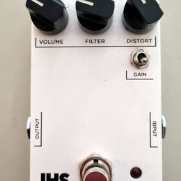 Bílý kytarový efekt s nápisem DISTORTION. Na horní straně jsou tři černé otočné ovnovky s popisky VOLUME, FILTER a DISTORT, dále je zde přepínač GAIN…