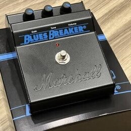 Černý kytarový efekt pedál značky Marshall s nápisem Blues Breaker. Na horní straně jsou tři ovládací knoflíky s popisky Gain, Tone a Volume. V dolní…