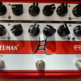 Červený kytarový předzesilovač s bílým horním panelem. Na červeném spodním panelu jsou nápisy Friedman, IR-J DUAL TUBE PREAMP a logo ve tvaru stylizo…