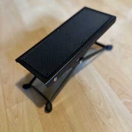 Černý skládací stojan s mřížkovým povrchem. Stojan je vyroben z kovových trubek a má čtyři nožičky s gumovými koncovkami. Na povrchu nejsou viditelné…