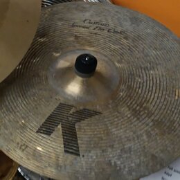 Zlatý cimbál s koncentrickými rýhami na povrchu. V horní části je nápis „Custom Special Dir Crash“, ve spodní části je velké černé písmeno „K“. Povrc…