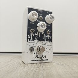 Bílý kytarový efekt s černým grafickým potiskem krajiny. Na horní straně jsou tři bílé otočné knoflíky s popisky Tone, Volume a Gain, dva přepínače o…