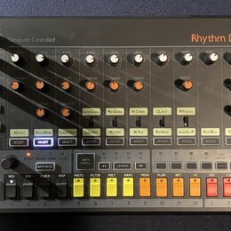 Šedý elektronický bicí automat s nápisem Rhythm Designer RD-8 a Computer Controlled. Zařízení obsahuje řadu bílých a oranžových otočných potenciometr…