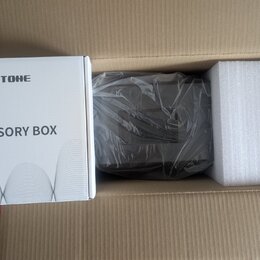 V hnědé kartonové krabici se nachází bílé papírové balení s nápisy HOTONE a ACCESSORY BOX. Vedle něj je tmavý, pravděpodobně plastový předmět zabalen…