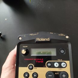 Černý spouštěcí modul s dorém panelu. Na horní straně je bílý nápis Roland a označení konektorů: OUTPUT L/MONO, R, TRIG IN 1, TRIG IN 2 a DC IN PSD A…