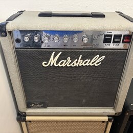 Kytarový zesilovač značky Marshall v krémovém vinylu s černou přední mřížkou. Na ovládacím panelu jsou knofíky a přepínače s nápisy: INPUT, GAIN, VOL…