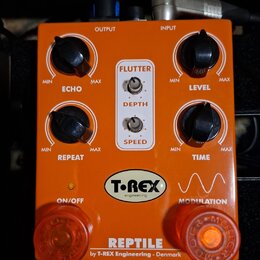 Oranžový kytarový efekt s nápisem REPTILE by T-REX Engineering - Denmark. Na horní straně jsou čtyři černé otočné ovladače s popisky ECHO, LEVEL, REP…