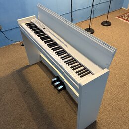 Bílé digitální piano s klasickým provedením a přívodním kabelem. Pod klaviaturou je umístěn černý pedál. Na ovládacím panelu jsou viditelné tlačítka…