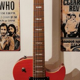 Červená elektrická kytara s tvarem připomínajícím Les Paul, umístěná na nástěnním držáku. Na hlavě je bílý nápis Washburn a logo ve tvaru stylizované…