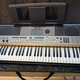 Stříbrný digitální klavír v černé přepravní tašce s přiklopnou hudební notovou deskou. Na přístroji je viditelné logo YAMAHA a označení modelu PSR-E4…