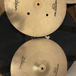 Dva mosazné činely typu hi-hat položené na černém obalu. Horní činel má nápisy Zildjian a BOTTOM QUICK BEAT HI HAT 14"35cm. Dolní činel nese nápisy Z…