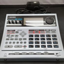 Stříbrný digitální doprovodný modul s nápisem BOSS DrRhythm DR-880. Zařízení má horní panel s ovládacími knoflíky, displejem a pravým volitkem, spodn…