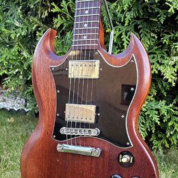 Elektrická kytara s hnědým dřevěným tělem a tmavým hnedým plechtrátem. Nástroj má dva humbuckery s kovovými kryty, čtyři otočné knoflíky a přepínač s…