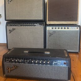 Fotografie zobrazuje pět kytarových komb značky Fender. V horní řadě je černý zesilovač s nápisem Deluxe Reverb Amp a béžový zesilovač s nápisem Fend…