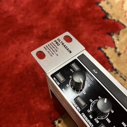 Detailní záběr na horní část stříbrného mikrofonního předzesilovače s černým předním panelem. Na horní kovové části je nápis ULTRAGAIN PRO AUDIOPHILE…
